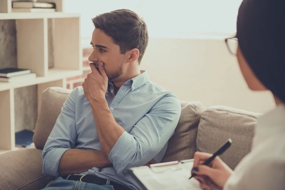 man thinking in therapy while counselor takes notes
