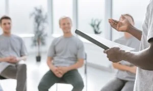 Attachment options… man reading from a notebook in front of group of men sitting