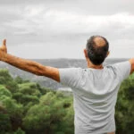 man standing in the mountains and stretching his arms open and above his head