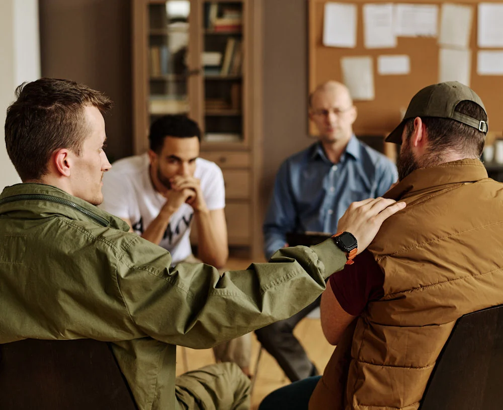One of attendants keeping hand on shoulder of upset man while comforting him 12-Step Program