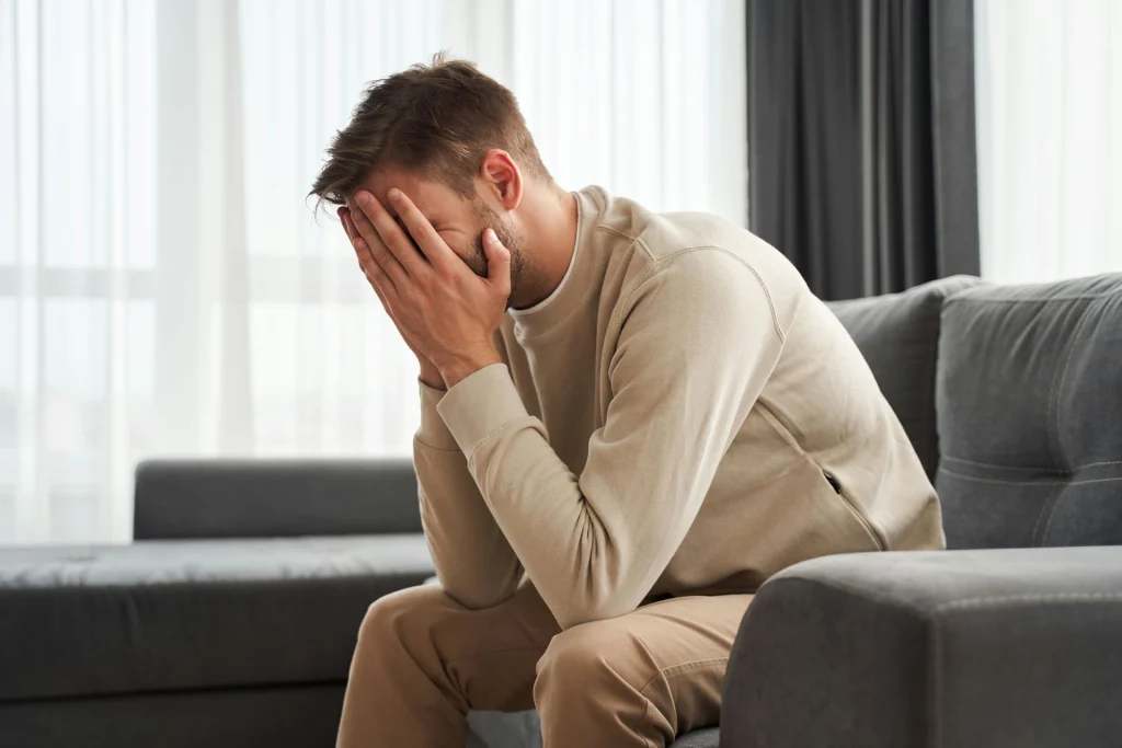 Man sitting with head in hands, representing barriers like stigma, fear, and shame that keep men from seeking addiction treatment.
