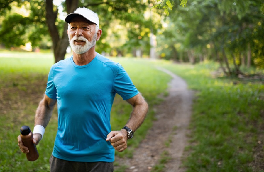 older man in blue shirt exercising by running on a path